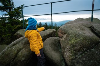 The child is standing between the boulders and is pointing at something in the distance. Polish mountains