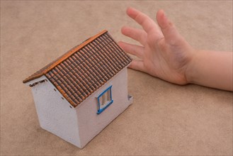 Little model house and a hand on a light brown color background