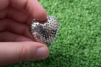 Silver color metal heart shape icon in hand on green sand