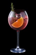 Cold sangria with orange and rosemary in a wine glass isolated on black background
