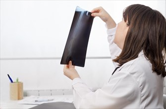Young female doctor in profile looking at a patients x-ray with a white background