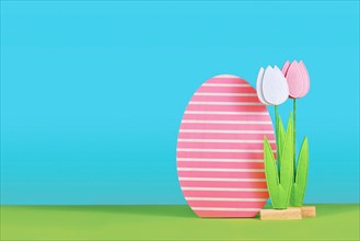 Easter arrangement with felt spring flowers and wooden easter egg on side of blue background