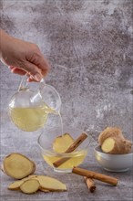 Womans hand pouring a cup of fresh ginger tea with cinnamon and lemon