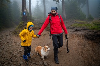 Mum and her little son go on a mountain trail in wet autumn weather. They are accompanied by a dog. Polish mountains
