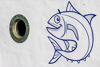 Detail of a white fishing boat with a round porthole and a drawing of a large fish