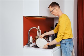 Middle-aged man washing plate after dinner in kitchen in the evening