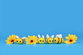 Cute felt bees and yellow flowers in a row on blue background with copy space