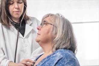 Young female doctor auscultating a patient with her stethoscope against a white background