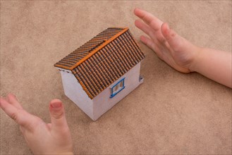 Little model house and a hand on a light brown color background