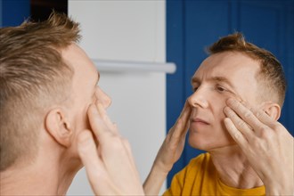 Concentrated man massaging and rubbing lotion under his eyes. Male aging problem