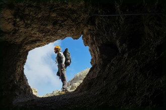 Tourist with equipment is standing in a hole in the rock with blue sky in the background. Dolomites