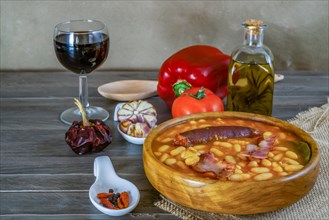 White beans stewed with bacon and chorizo in a wooden bowl with all its ingredients