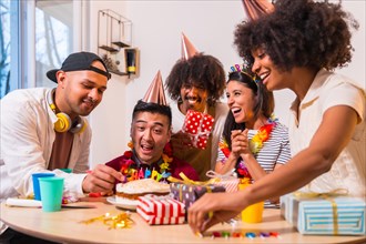 Multi-ethnic group of friends at a birthday party on the sofa at home with a cake and gifts