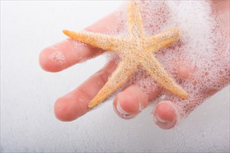 Hand holding starfish in water covered with foam
