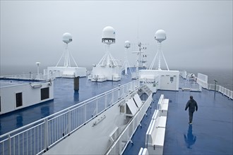 A man in drizzle and foggy weather on the deck of the ferry Norroena with marine electronics and the North Atlantic