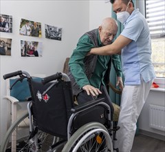Carer helps old man stand up in a nursing home