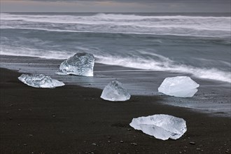 Melting blocks of ice washed on beach along the Atlantic Ocean coastline at Breidamerkursandur black sands in winter