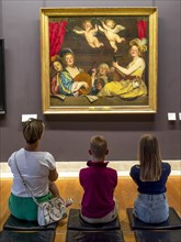 A woman and two children look at a picture on a wall in the Louvre