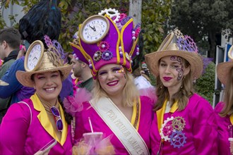 Three masked smiling girls in pink clothes with clock hats at the carnival in the city of Rijeka