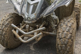 Black front rubber tires covered with dried mud on All Terrain Vehicle parked on gravel road surface