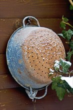 Snow-covered kitchen sieve on a wooden wall