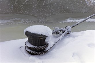 Snow-covered bollard at the harbour edge