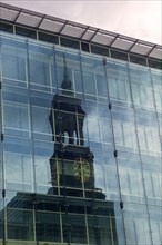 The tower of St. Michaels Church is reflected in the facade of a high-rise office building