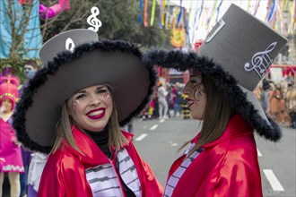 Two smiling girls in red coats with a keyboard and big top hats on their heads at the carnival in the city of Rijeka