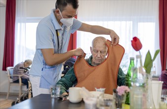 Carer puts a bib on a man in a nursing home