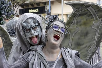 Young smiling woman with wings in grey and the devil masked at the carnival in the city of Rijeka