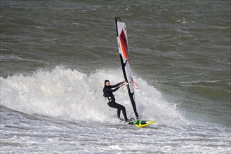 Recreational windsurfer in black wetsuit practising classic windsurfing along the North Sea coast in windy weather during winter storm
