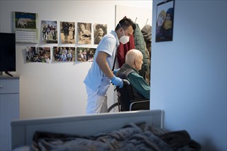 Geriatric nurse pushing a wheelchair through a door in a nursing home