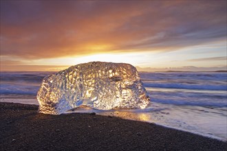 Melting block of ice washed on beach along the Atlantic Ocean coastline at Breidamerkursandur black sands in winter