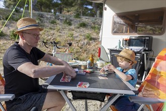 Subject: Holiday. Grandfather and grandchild sitting at the table on a campsite in Croatia playing a card game