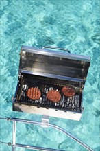 Charcoal grill with hamburgers at the railing of a sailing catamaran