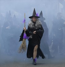 A witch in black and with a broom and behind everything in the smoky mist at the carnival in the city of Rijeka