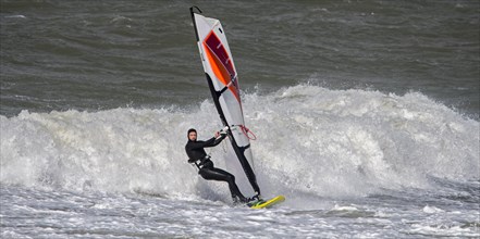 Recreational windsurfer in black wetsuit practising classic windsurfing along the North Sea coast in windy weather during winter storm