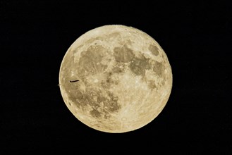 A plane looms in front of the so-called strawberry moon looms as it rises in Berlin