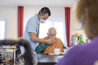 Carer helps a man to drink in a nursing home
