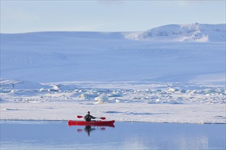 Kayaker in red kayak on the Joekulsarlon glacier lagoon in winter
