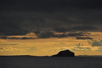 Bass Rock and its lighthouse at sunset with rain clouds