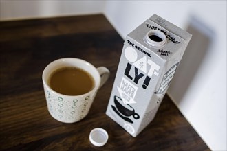 Symbolic photo on the subject of oat milk in coffee. A carton of Oatly Barista oat milk stands next to a cup of coffee. Berlin