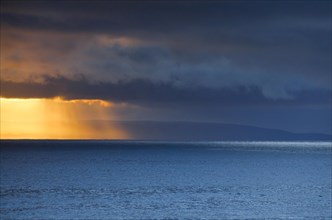 Evening sun breaks through low-lying rain clouds over the Summer Isles and the open waters of the blue Atlantic