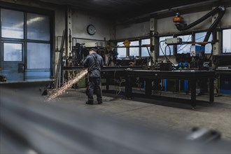 A metal worker works on a steel beam with a cut-off grinder