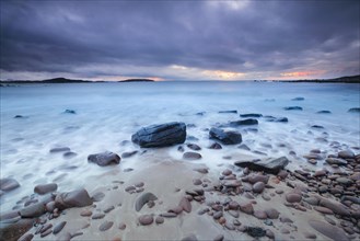 Dramatic cloudy sky at sunset on a sandy beach strewn with round stones near Achiltibuie on the west coast of Scotland