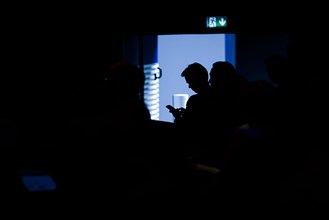 A man sits in the audience of an event and types on his smartphone. Berlin