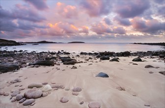 Purple coloured cloudy sky at sunset on a sandy beach strewn with round stones near Achiltibuie on the west coast of Scotland