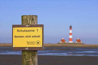 Mudflat and Wadden Sea National Park sign in front of the lighthouse Westerhever in spring