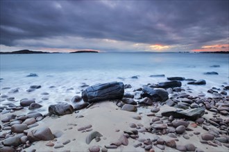 Dramatic cloudy sky at sunset on a sandy beach strewn with round stones near Achiltibuie on the west coast of Scotland