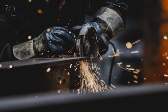 A metal worker works on a steel beam with a cut-off grinder